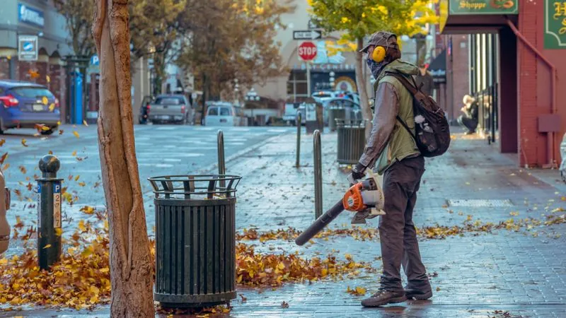 Worker clearing fallen leaves with a backpack blower