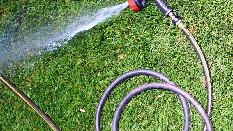 Hose spraying treatment across a green lawn